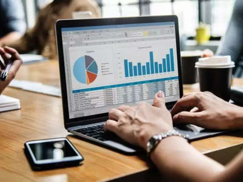 Laptop computer open to circle and bar graphs on a desk with hands typing